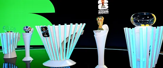 Scène du tirage au sort de la CDM 2026 avec la Coupe du Monde et les bols transparents alignés sur des présentoirs lumineux