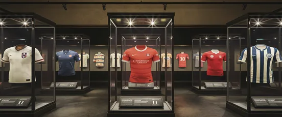 Exposition de maillots de football iconiques présentés dans des vitrines de musée, symbolisant 25 ans d’histoire et de légendes